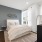 A modern bedroom with a plush upholstered bed, soft neutral decor, a large window offering natural light and scenic views, and minimalist furnishings.