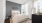 A modern bedroom with a plush upholstered bed, soft neutral decor, a large window offering natural light and scenic views, and minimalist furnishings.