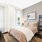 A sophisticated bedroom featuring a plush bed with neutral bedding, abstract wall art, bedside lamps, and a large closet leading to a private bathroom.