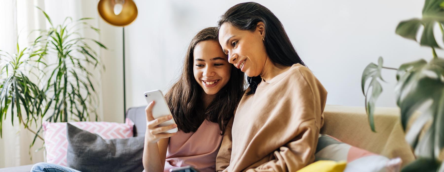 a couple of women sitting on a couch looking at a phone