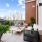 A beautifully designed outdoor patio featuring a comfortable seating area, a dining table, lush greenery, and a scenic view of the surrounding community.