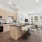 A sleek kitchen with wood cabinetry, stainless steel appliances, and a central island with bar seating, seamlessly connected to a sunlit living and dining area.