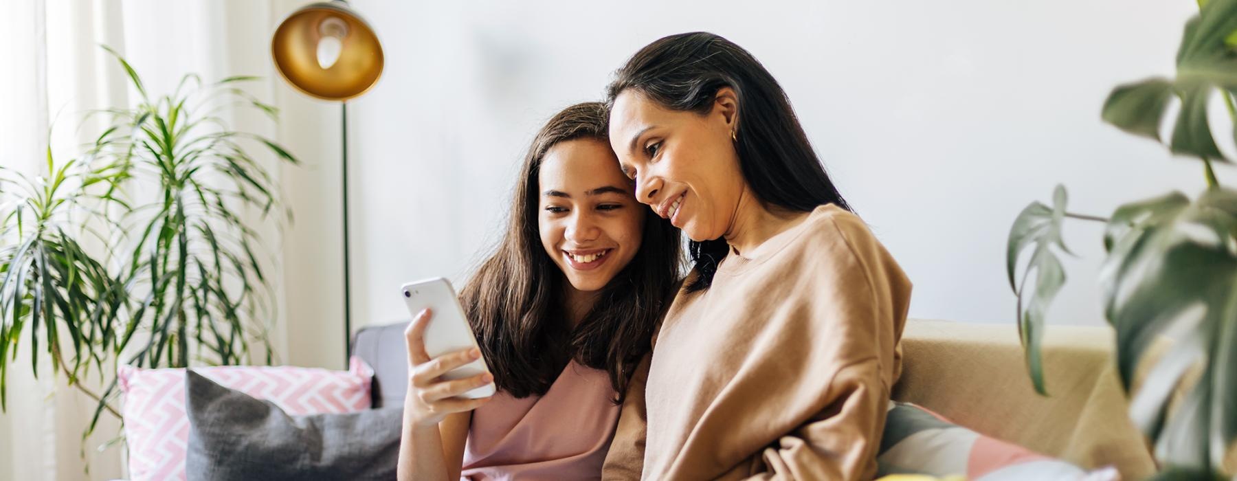 a couple of women sitting on a couch looking at a phone